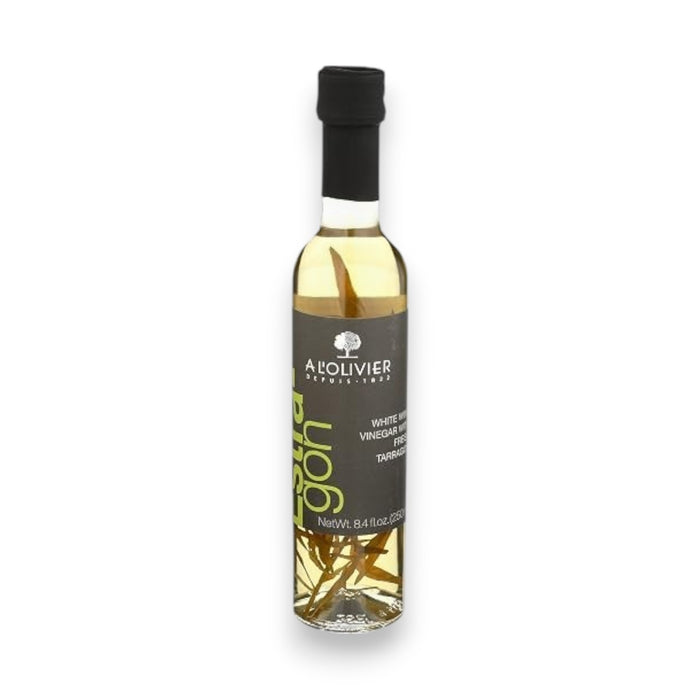 A clear bottle of A L’OLIVER - WHITE WINE VINEGAR TARRAGON from ATALANTA CORPORATION, made with white wine vinegar and infused with aromatic tarragon, features a black cap and a dark label with white and green text, standing on a white background.