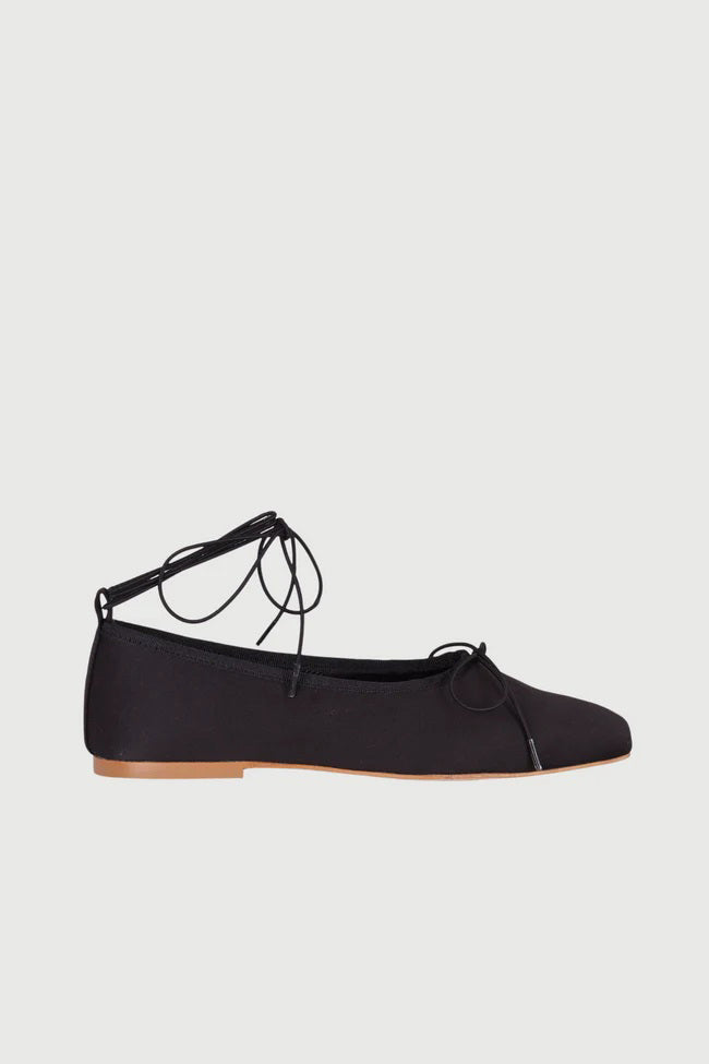 The AUGUSTA - SIENNA BALLET FLAT by AUGUSTA, handcrafted in Spain, showcases a silver finish with a front bow, low brown sole, and heel pull tab, displayed in side profile against a plain light background.