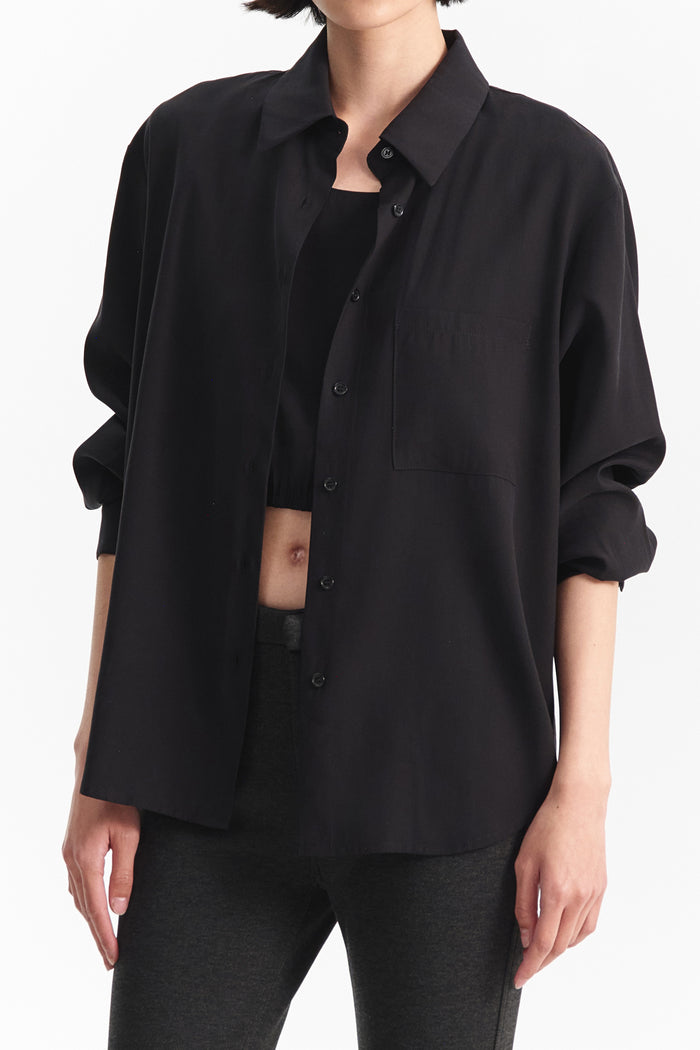 The ELEH - THE ESSENTIAL BLACK SHIRT, featuring long sleeves, a pointed collar, and chest pocket, hangs against a white background—ideal for those who value minimalist luxury.