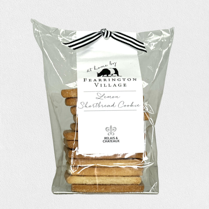 A white plate with rectangular, golden-brown FEARRINGTON HOUSE Fearrington Signature Collection - Housemade Lemon Shortbread Cookies sits on a wooden surface beside a beige cloth and a small green plant.