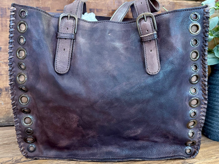 Grommeted leather tote bag, front view with buckled straps and metal eyelets