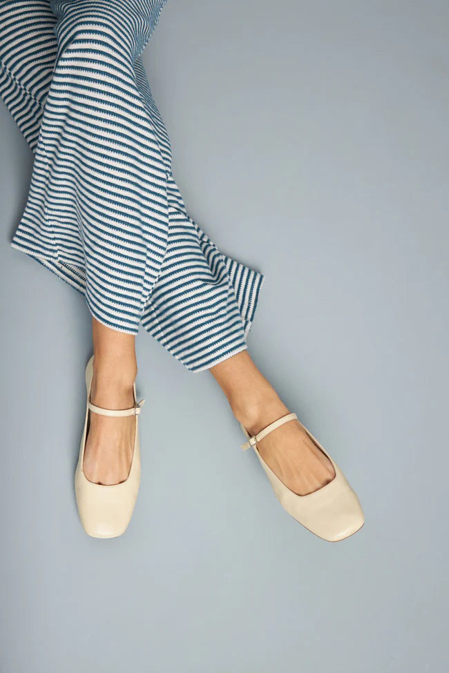 The AUGUSTA - JULIETA MARY JANE by AUGUSTA is a black leather Mary Jane flat with a thin strap and buckle, light brown sole, and subtle square toe, handcrafted in Spain and shown on a light gray background.