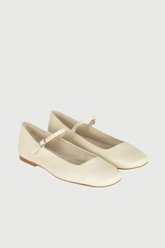 The AUGUSTA - JULIETA MARY JANE by AUGUSTA is a black leather Mary Jane flat with a thin strap and buckle, light brown sole, and subtle square toe, handcrafted in Spain and shown on a light gray background.