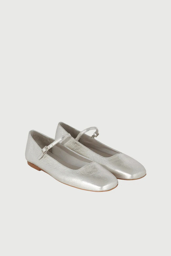 The AUGUSTA - JULIETA MARY JANE by AUGUSTA is a black leather Mary Jane flat with a thin strap and buckle, light brown sole, and subtle square toe, handcrafted in Spain and shown on a light gray background.