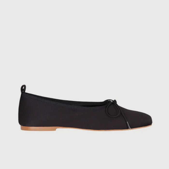 The AUGUSTA - SIENNA BALLET FLAT by AUGUSTA, handcrafted in Spain, showcases a silver finish with a front bow, low brown sole, and heel pull tab, displayed in side profile against a plain light background.