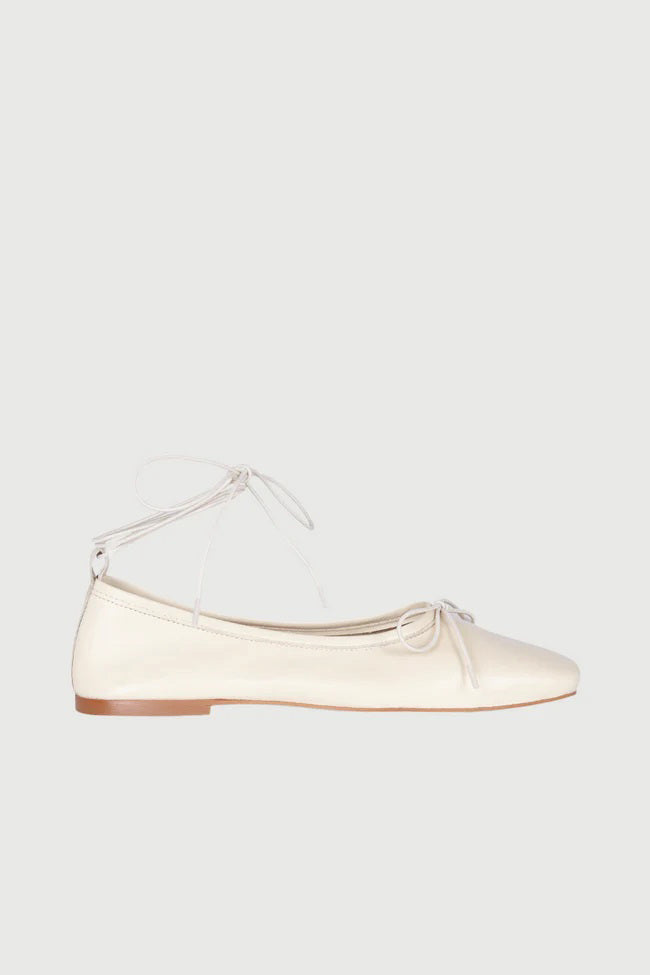 The AUGUSTA - SIENNA BALLET FLAT by AUGUSTA, handcrafted in Spain, showcases a silver finish with a front bow, low brown sole, and heel pull tab, displayed in side profile against a plain light background.