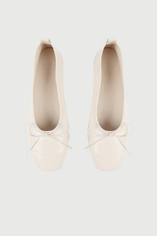The AUGUSTA - SIENNA BALLET FLAT by AUGUSTA, handcrafted in Spain, showcases a silver finish with a front bow, low brown sole, and heel pull tab, displayed in side profile against a plain light background.