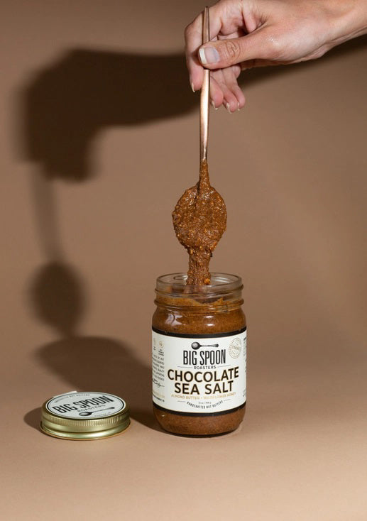 A jar of BIG SPOON ROASTERS Chocolate Sea Salt Almond Wildflower Nut Butter, featuring a gold lid and a white label with black and gold text; handcrafted with sea salt.