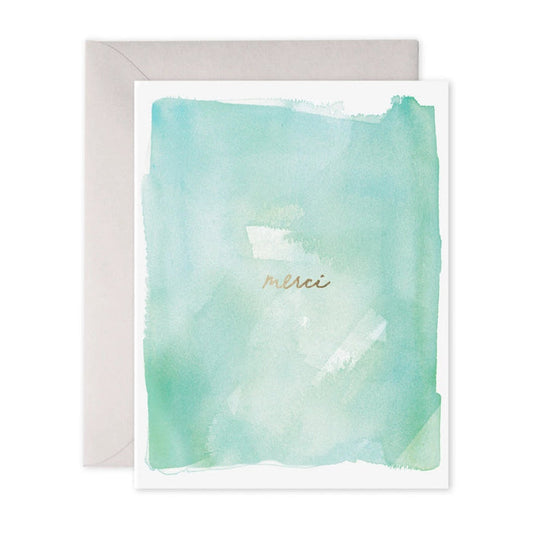 The E. Frances Paper Merci Card showcases a pastel green and blue watercolor background, with "merci" scripted in gold cursive. It exudes positive energy and comes with a light gray envelope—perfectly blending Ali's artistry and sentiment.