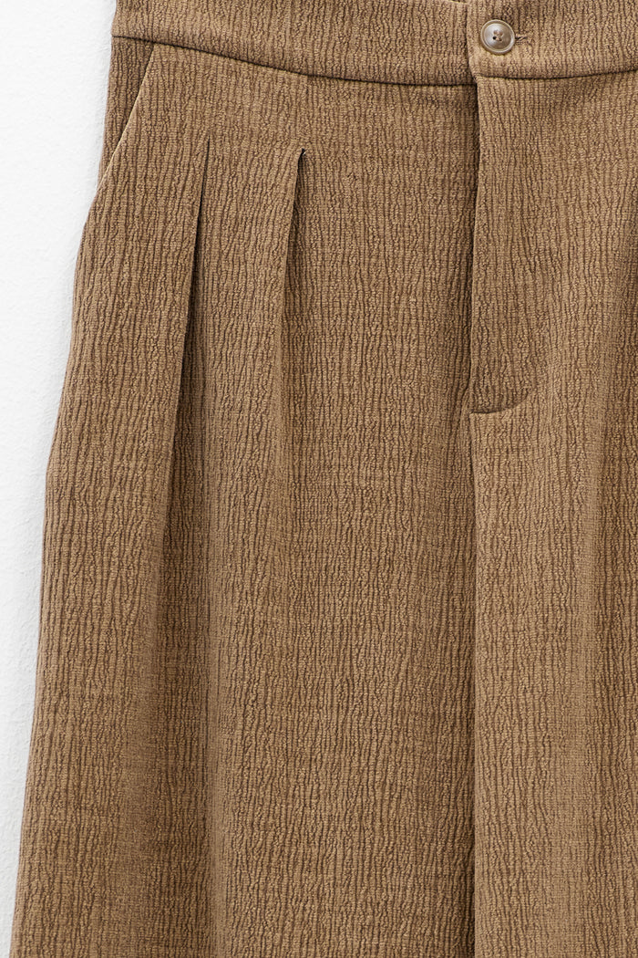 A person wearing ELEH CLASSIC WIDE LEG TROUSERS and a matching brown corduroy jacket, paired with brown shoes and large sunglasses, stands against a plain white background with hands in pockets.