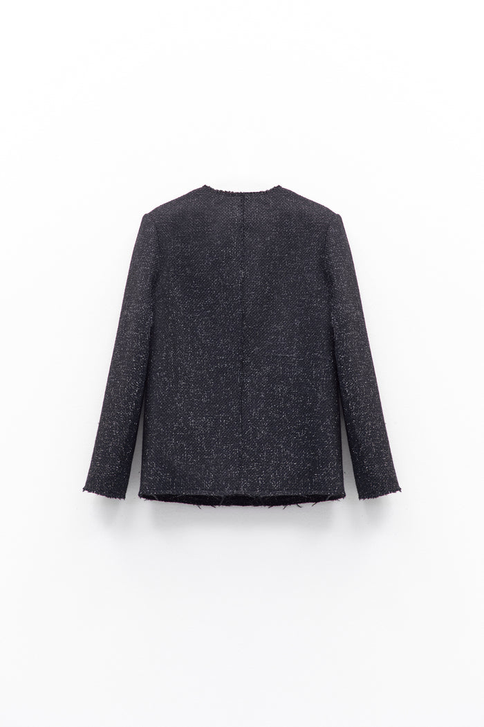 A person wears the ELEH - TWEED JACKET by ELEH, featuring textured black fabric and large front pockets, paired with dark pants and a black clutch with silver chain, against a white background.