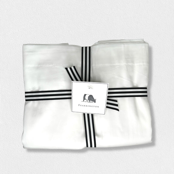 The FEARRINGTON LIFESTYLE BEDDING COLLECTION - FRETTE PILLOWCASES S4 by Frette North America features luxury white cotton sateen pillowcases, elegantly bundled with a black and white striped ribbon and finished with a "Fearrington" tag.