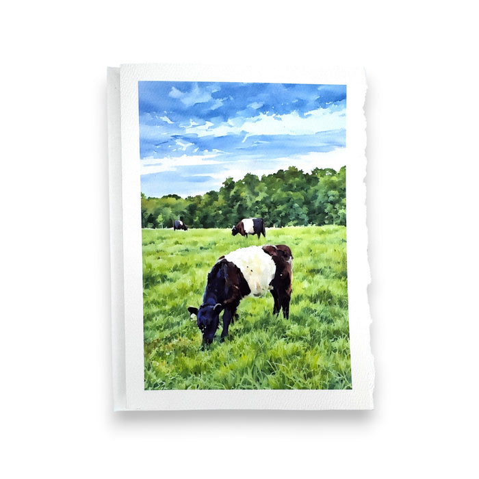The FEARRINGTON SIGNATURE COLLECTION - WATERCOLOR GREETING CARD "GRAZING" by PICTURE SALON features a black and white cow in a green field with more cows, trees, and blue sky, printed on torn-edged paper.