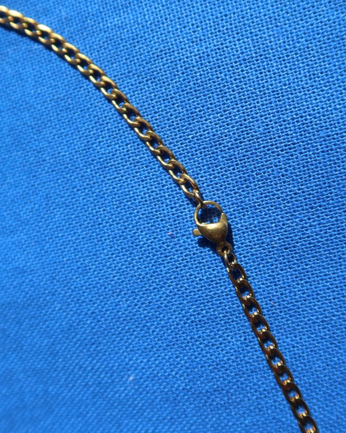 Close-up of a lobster claw clasp and gold necklace chain with a clasp on a blue fabric background