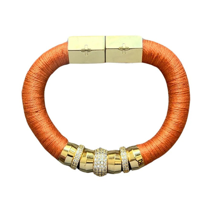 The HOLST & LEE LUXE CLASSIC BRACELET features a gold clasp, orange thread wrap, and gold-plated cylindrical beads embellished with rhinestones, showcased against a plain white background.