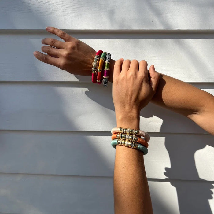 The HOLST & LEE LUXE CLASSIC BRACELET features a gold clasp, orange thread wrap, and gold-plated cylindrical beads embellished with rhinestones, showcased against a plain white background.