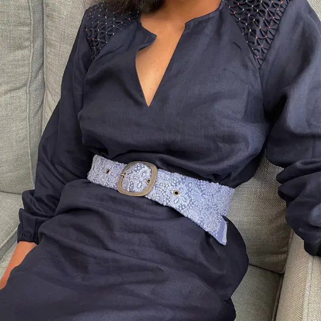 The JENNY KRAUSS - AZURE SEAS EMBROIDERED WOOL BELT by JENNY KRAUSS features an embroidered floral pattern, an adjustable waist, and a silver rectangular buckle, shown coiled on a white surface.