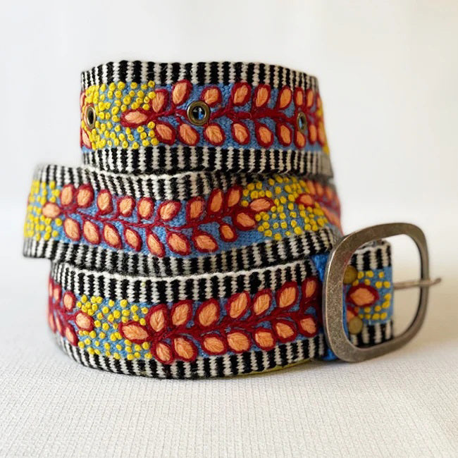 The JENNY KRAUSS - GROWING SEASON BELT by JENNY KRAUSS is a coiled, handcrafted Peruvian belt with black and white stripes, red and yellow leaf and dot embroidery, silver metal buckle, shown on a white surface.