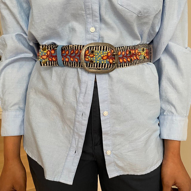 The JENNY KRAUSS - GROWING SEASON BELT by JENNY KRAUSS is a coiled, handcrafted Peruvian belt with black and white stripes, red and yellow leaf and dot embroidery, silver metal buckle, shown on a white surface.