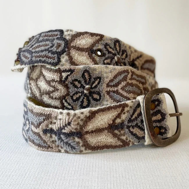 The JENNY KRAUSS Monochromatic Belt in Cream, handcrafted in Peru with floral and geometric embroidery in beige, brown, and gray, features a metal buckle and is shown coiled on a light surface.