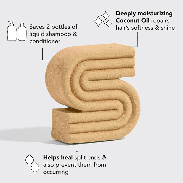 The KITSCH - Coconut Oil Deep Moisturizing Shampoo Bar, ideal for curly and kinky hair, is displayed alongside a coconut half, palm leaf, herbs, and a sample on a beige surface. The packaging highlights the inclusion of coconut oil as a key ingredient.