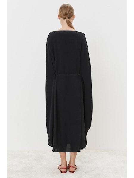 A person stands gracefully on a light-colored floor, wearing the MEIMEIJ Silk Blend Dress with cape-like sleeves, showcasing a modern classic look. The outfit is paired with red, open-toed flat shoes against a simple white backdrop.