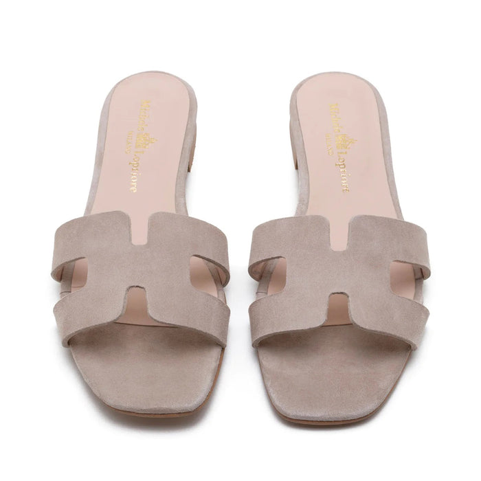 The MICHELE LOPRIORE - H SLIDE is a brown leather sandal with two wide straps, including one with a rectangular cutout, featuring a flat wooden sole. Made in Italy by MICHELE LOPRIORE, it's shown on a white background.