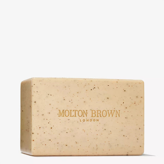 A rectangular beige MOLTON BROWN RE-CHARGE BLACK PEPPER BODY SCRUB BAR (250g) with small dark specks and "MOLTON BROWN LONDON" in gold across the front.