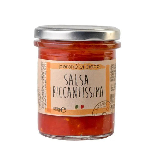A 180g glass jar of Perche Ci Credo Salsa Piccantissima Extra Spicy Spread by Zia Pia Imports features a silver lid, a beige label with Italian flag colors, and showcases artisanal Apulian tomatoes and chili for authentic heat.