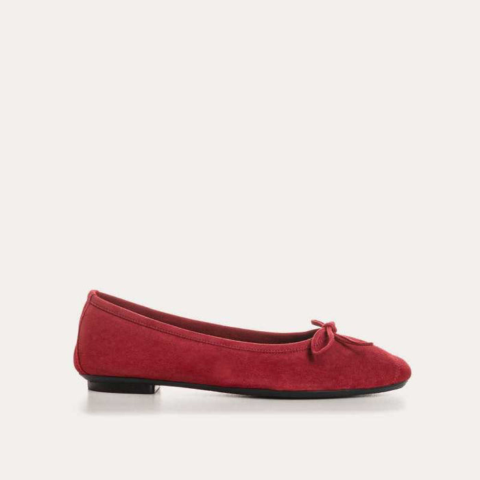 A person wearing blue jeans and REQINS - HARMONY Suede Ballerina Flats in cerise stands on a light-colored floor.