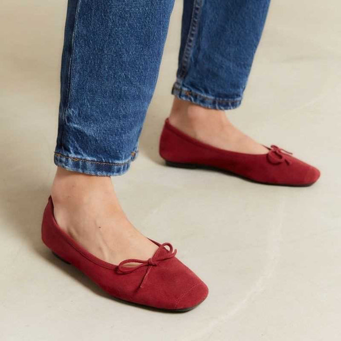 A person wearing blue jeans and REQINS - HARMONY Suede Ballerina Flats in cerise stands on a light-colored floor.