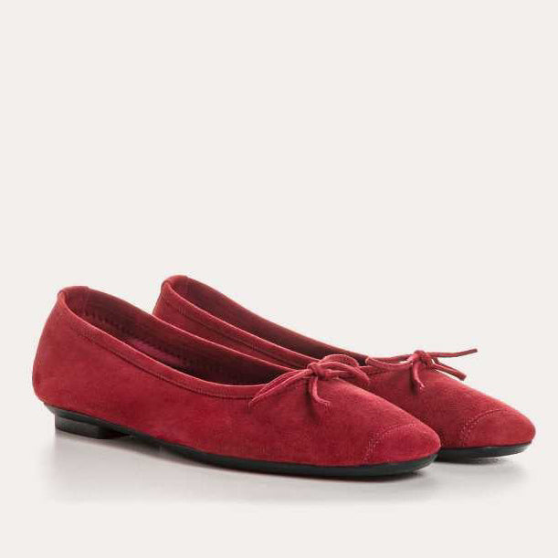 A pair of red suede ballet flats with small bows on the toes, displayed on a light background.