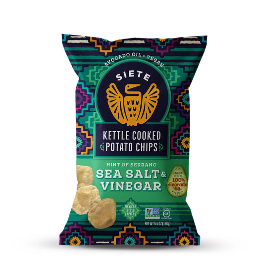 A vibrant bag of SIETE FOODS KETTLE CHIPS SEA SALT VINAGAR WITH A HINT OF SERRANO shows the eagle logo, bold patterns, crispy chips, and highlights vegan status and avocado oil on the front.